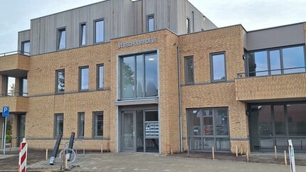 Vooraanzicht van een modern gebouw met bakstenen en houten gevel, voorzien van grote ramen en een bord met de tekst “Verschuurhoeve"